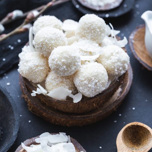 A vertical shot of raw raffaello in a wooden bowl with coconut chunks and a wooden spoon